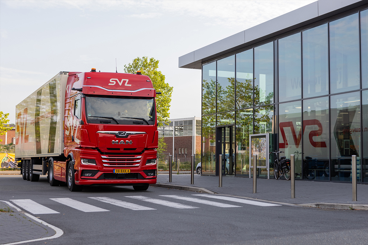 Een rode MAN-trekker met SVZ-oplegger rijdt langs een modern bedrijfspand