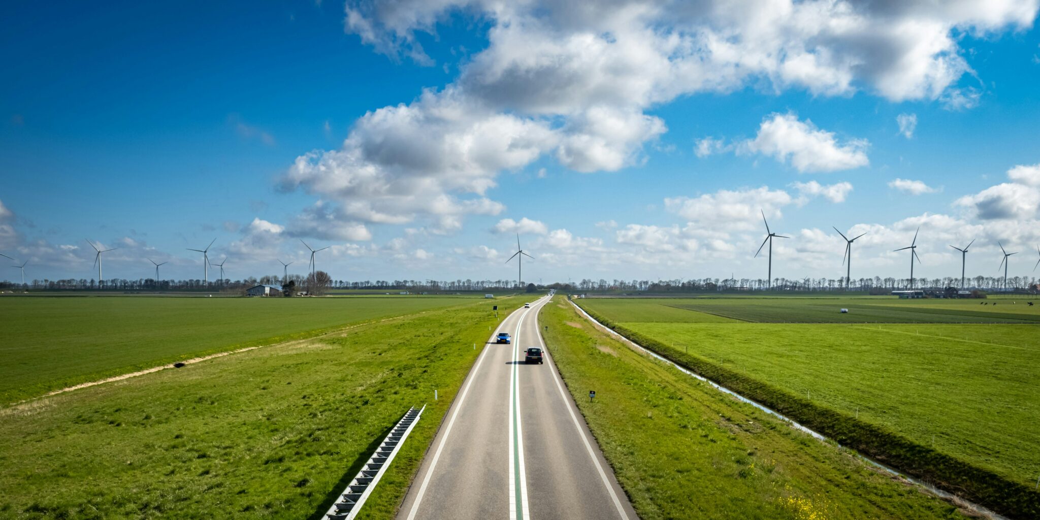 Tweebaansweg door Nederlands weiland, met windturbines aan de horizon